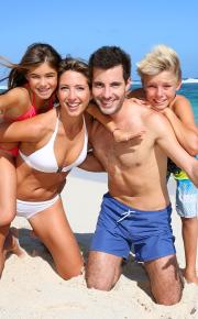 Famiglia felice in spiaggia, genitori e figli sorridenti.